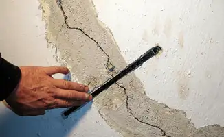 A wall with a large crack is being inspected by a professional in Tempe, AZ